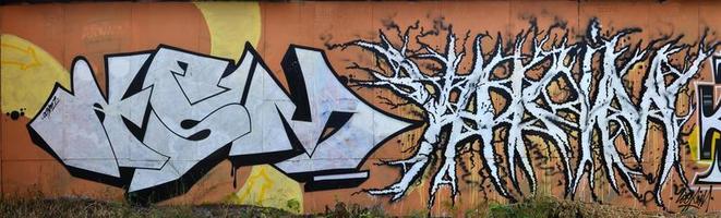 una foto de varias obras de arte de graffiti en la pared de metal. Los dibujos de graffiti están hechos con pintura blanca con contornos negros y tienen un fondo naranja. textura de pared con decoración de graffiti