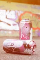 A few used spray cans with pink and white paint lie on the asphalt against the background of a painted wall in colorful graffiti drawings photo