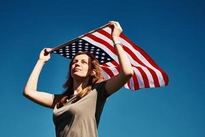 mujer sostiene la bandera de estados unidos contra el cielo azul foto