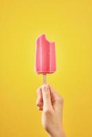 Bitten red frozen fruit ice cream popsicle on yellow background photo