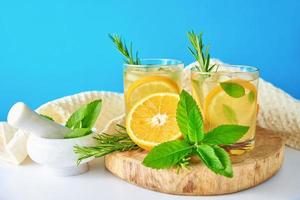 Glass of water with orange, mint and rosemary on blue background