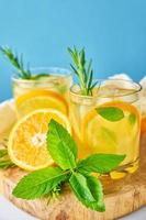 Glass of water with orange, mint and rosemary on blue background photo