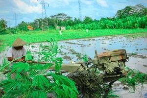 gianyar, indonesia - 06 de enero de 2023. un agricultor que está arando un campo usando una máquina de arado de arroz foto