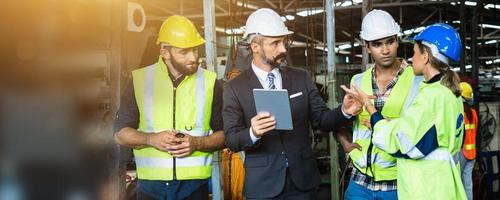 Industrial engineer and businessman in safety helmet working in factory, planning, discussing and training workers with tablet in metalwork place , teamwork and team concept photo