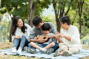 Happy family with grandma, mom with dad teaching son  playing guitar and sing a song in park, Enjoy and relax people picnic outside photo