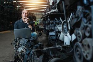 un hombre atractivo usa la comunicación por radio con otros afuera para revisar y reparar el mecánico de automóviles en el motor del automóvil en el garaje mecánico. servicio de reparación foto