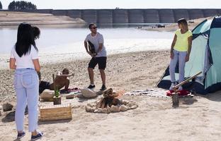 Happy friends camping party playing music and enjoying bonfire in nature and lake, photo