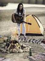 Portrait of a young woman playing guitar near bonfire by the lake photo