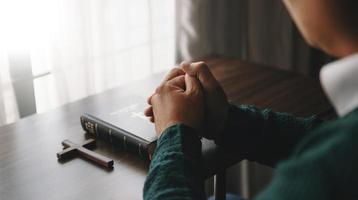 manos juntas en oración a dios junto con la biblia en el concepto cristiano y la religión, la mujer reza en la biblia sobre la mesa foto