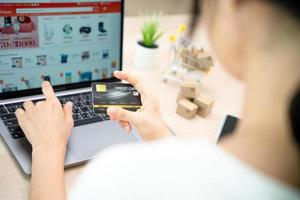 Woman use credit card to make online purchases on laptop. Online service. New normal shopping delivery. Online shopping-boxes or parcels are placed shopping carts. photo