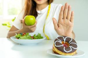 Women reject junk food or unhealthy foods such as doughnuts and choose healthy foods such as green apples and salads. Concept of fasting and good health.