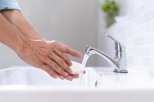 Men washing hands with soap and clean water in front of the bathroom sink to prevent the spread of germs. Washing hands with soap.