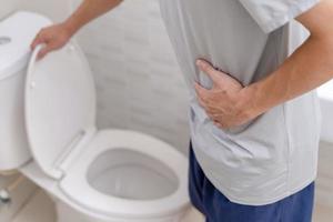 man standing has diarrhea and severely toxic food. Man touch belly in the bathroom. Abdominal pain, Diarrhea, Colon cancer concept photo