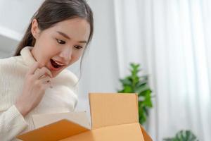 una mujer bastante asiática se siente sorprendida y mira interesada dentro de la caja de regalos. linda chica emocionada caja de regalo abierta. cumpleaños, celebración, navidad, festival de año nuevo, gracias, celebrar, día de san valentín, aniversario foto