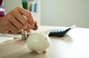 Businessman holding coins putting in piggy bank with a calculator and a pile of coins. Concept saving money for finance accounting photo