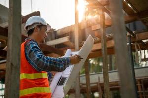 el hombre contratista revisa el dibujo del borrador del nuevo hogar. Se lee a los ingenieros los detalles de la construcción en el dibujo y se comparan en el sitio real. concepto ingeniero civil e inspector foto