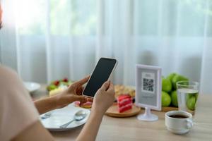 la mujer usa un teléfono inteligente para escanear el código qr para pagar en un café restaurante con un pago digital sin efectivo. elige menú y ordena acumula descuento. billetera electrónica, tecnología, pago en línea, tarjeta de crédito, aplicación bancaria foto