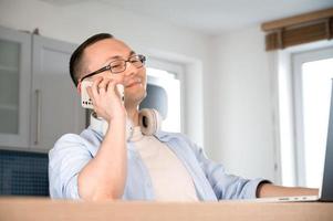 Asian man with phone and laptop. sitting down and talking over smartphone ordering something or discussing something with customer. photo