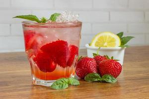 A refreshing summer drink with ice, strawberries and lemon on a wooden background. The concept of fruit drink. photo