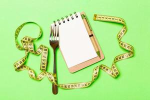 Fitness concept with empty space for your design on green background. Top view of notepad and fork surrounded with yellow measure tape photo