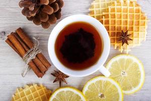 Cup of black tea with Christmas decor, lemon, pinecone, waffles, badian and cinnamon photo