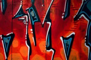 A fragment of detailed graffiti of a drawing made with aerosol paints on a wall of concrete tiles. Background image of street art in warm red color tones photo
