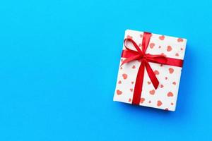 Gift box with red ribbon and heart on blue background, top view with copy space for text photo