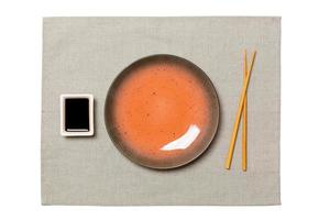 Empty round brown plate with chopsticks for sushi and soy sauce on grey napkin background. Top view with copy space for you design photo