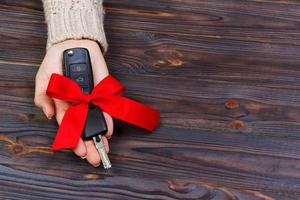 Car key with red bow in woomen hand on wooden background. Valentine's Day concept photo