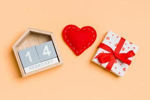 Composition of wooden calendar, holiday white gift boxes and red textile hearts on colorful background. The fourteenth of February. Valentine's day concept photo