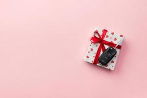 Car key on paper gift box with red ribbon bow and heart on table background. Holidays present top view concept photo