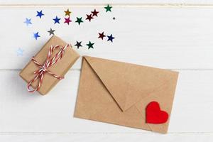 correo de sobre con corazón rojo y caja de regalo sobre fondo blanco de madera. tarjeta de san valentín, amor o concepto de saludo de boda foto