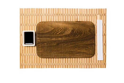 Empty rectangular brown wooden plate with chopsticks for sushi and soy sauce on yellow bamboo mat background. Top view with copy space for you design photo