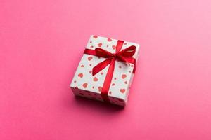 Gift box with red ribbon and heart on pink background, top view with copy space for text photo