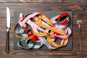 Top view of heap of colorful measuring tapes in plate on wooden background. Diet concept with copy space photo