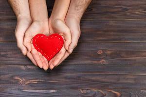 Love, family concept. Close up of man and woman hands holding red rubber heart together photo