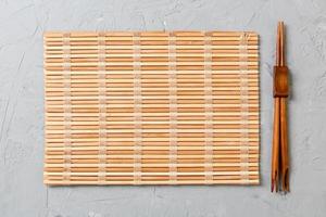 two sushi chopsticks with empty bamboo mat or wood plate on stone Background Top view with copy stace photo