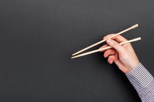 Male hand with chopsticks on black background. Traditional asian food with emty space for your design photo