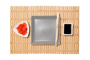 Empty gray square plate with chopsticks for sushi, ginger and soy sauce on yellow bamboo mat background. Top view with copy space for you design photo