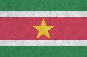 Suriname flag depicted in bright paint colors on old relief plastering wall. Textured banner on rough background photo