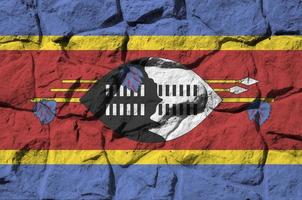 Swaziland flag depicted in paint colors on old stone wall closeup. Textured banner on rock wall background photo