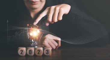 New Year 2023 Beginning Concept,,concept with innovation and inspiration, innovative technology in science concept and modern business development,creative idea,man pointing light bulb on table photo