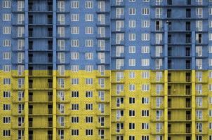 Ukraine flag depicted in paint colors on multi-storey residental building under construction. Textured banner on brick wall background photo