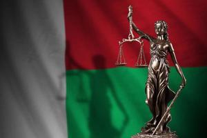 Madagascar flag with statue of lady justice and judicial scales in dark room. Concept of judgement and punishment photo