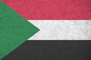 Sudan flag depicted in bright paint colors on old relief plastering wall. Textured banner on rough background photo