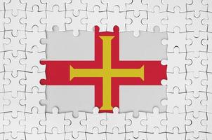 Guernsey flag in frame of white puzzle pieces with missing central part photo