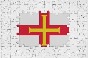 Guernsey flag in frame of white puzzle pieces with missing central part photo