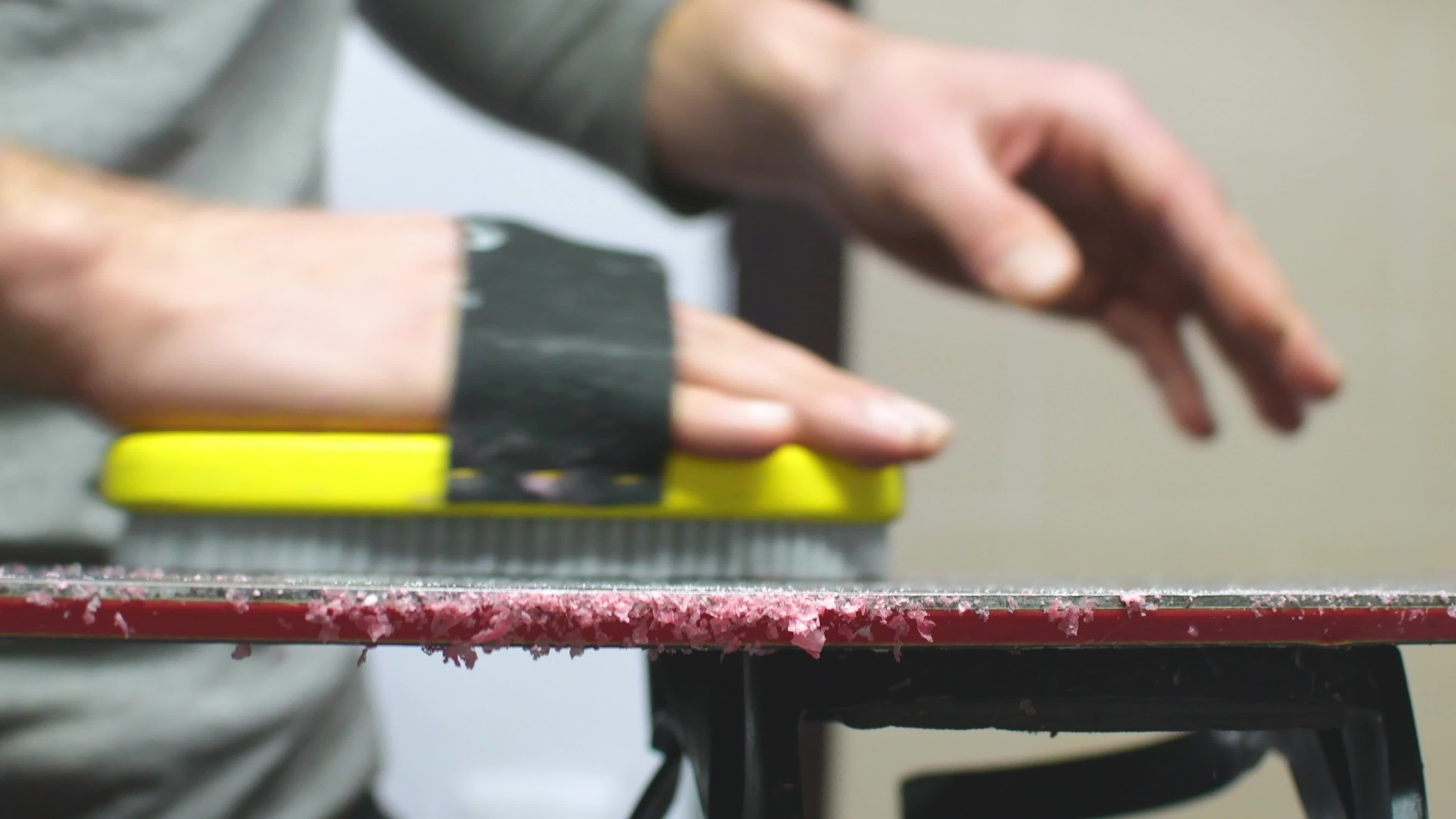 Hand hold brush and brushing wax on snowboard close up. Snowboard