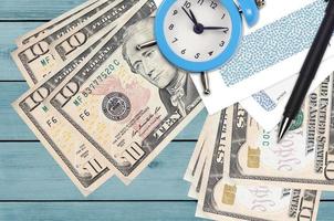 10 US dollars bills and alarm clock with pen and envelopes. Tax season concept, payment deadline for credit or loan. Financial operations using postal service photo