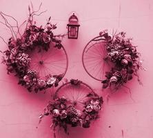 Decoration urban art object from bicycle wheels and flowers on wall Image toned in Viva Magenta, color of the 2023 year photo
